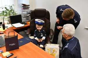 Kubuś siedzący za biurkiem na miejscu naczelnika, obok niego Zastępca Komendanta Wojewódzkiego Policji w Katowicach, insp. Mariusz Krzystyniak oraz naczelnik