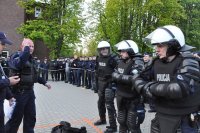 Trzech policjantów ubranych w sprzęt ochrony osobistej. Po lewej stronie policjant sędzia ze stoperem odmierza czas. W drugim planie policjant machający ręką w dół.