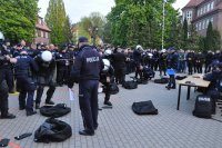 Kilka grup policjantów - drużyn,  zakładających na siebie sprzęt ochrony osobistej widok z dalszej perspektywy. Po prawej stronie stolik sędziowski i policjanci oceniający przebieg konkurencji. W tle widać dopingujących policjantów.