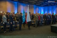 Sala obrad. Wprowadzenie Sztandaru Policji. Uczestnicy stoją.