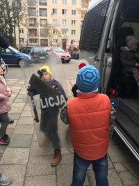 Chłopiec trzymający dużą tarczę przed radiowozem w towarzystwie innych dzieci.