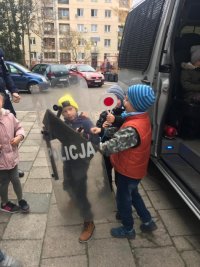 Dzieci przed radiowozem policyjnym bawią sią w policjantów.