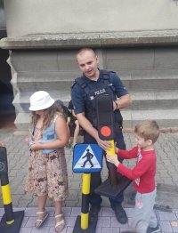 Policjant tłumaczący dwójce dzieci, jak działa sygnalizacja świetlna.