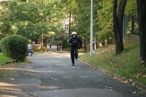 Policjant w pełnym sprzęcie PZ biegnie pod górę w kierunku hali sportowej.