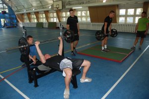 Policjanci w konkurencji wyciskania sztangi leżąc i martwego ciągu na hali sportowej.