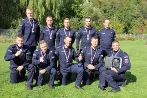 Zdjęcie zbiorowe dziesięciu policjantów w mundurach. Ma szyjach mają założone medale na wstążkach. Jeden trzyma w ręku statuetkę umieszczoną w skrzyneczce.