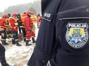 Na pierwszym planie ujęcie kurtki z umundurowania policyjnego funkcjonariusza Wydziału Doboru i Szkolenia Komendy Wojewódzkiej Policji w Katowicach, w tle uczestnicy szkolenia w pełnym ubiorze i sprzęcie.