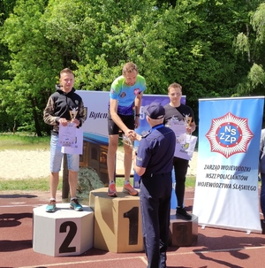 Zawodnicy z pierwszych trzech miejsc na podium. Pierwszy Zastępca Komendanta Wojewódzkiego Policji w Katowicach inspektor Mariusz Krzystyniak gratuluje zwycięzcy.