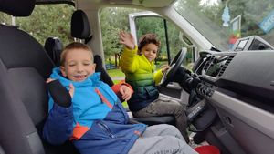 2 przedszkolaków siedzi na przednich siedzeniach radiowozu typu furgon.