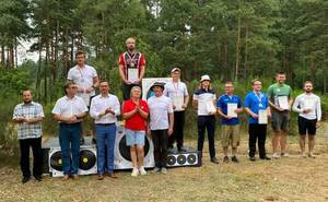 Zdjęcie. Zdjęcie grupowe z zawodów w łucznictwie polowym. Sierżant Adam Ścibski stoi na najniższym stopniu podium z medalem na szyi i dyplomem w rękach.