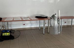 Tarcza ochronna, plecakowy miotacz pieprzu oraz wyłożone na stole zdjęcia wyposażenia i uzbrojenia używanego w Oddziale.