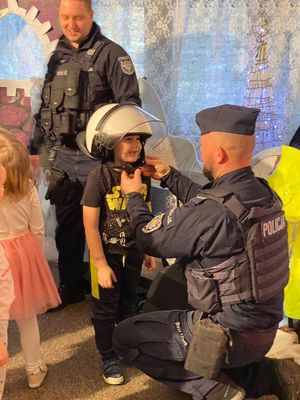 Policjant pomaga jednemu z przedszkolaków założyć i zapiąć kask ochronny.