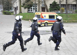 3 policjantów w sprzęcie PZ biegnie w kierunku stanowiska z bronią gładkolufową.