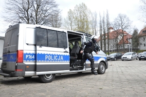 Policjant w sprzęcie PZ dynamicznie wyskakuje z radiowozu typu furgon.
