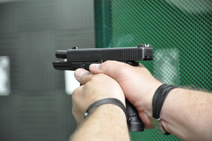 Zbliżenie na pistolet Glock pod oddaniu strzału z zamkiem w tylnym położeniu. Na ujęciu widać dym.