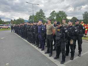 Grupa osób w mundurach stoi w szyku. Widok z boku szyku obejmujący całą grupę około 60 osób. Widoczny policjant w polskim mundurze.