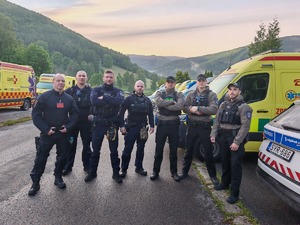 Zdjęcie pozowane. Grupa sześciu osób, w tym trzech policjantów w polskich mundurach. W tle ambulanse medyczne w żółtym kolorze.