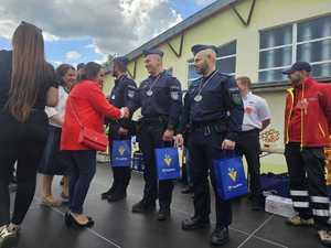 Na zdjęciu trzech policjantów w polskich mundurach. Mają na szyi medale. Zdjęcie na tle budynku. Dwie osoby bez munduru składają gratulacje.