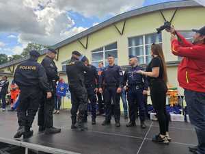 Na zdjęciu trzech policjantów w polskich mundurach. Moment zakładania medali na szyję policjantów przez innych trzech policjantów. Z boku osoba robiąca zdjęcie.
