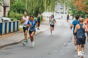 Pierwsi trzej zawodnicy podczas biegu. Obok widziani od tyłu inni zawodnicy.