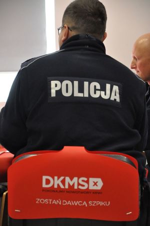 Policjant w polarze z napisem Policja na plecach siedzi na krześle z nakładką Fundacji.